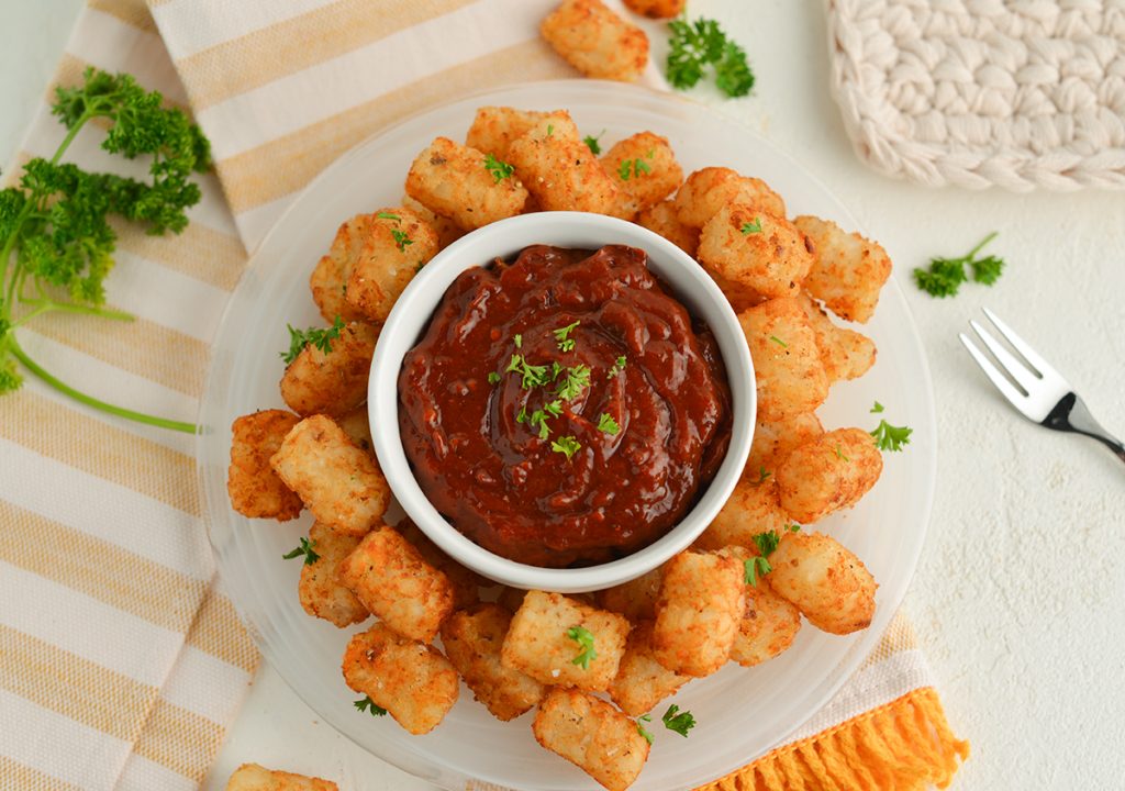 overhead shot of chipotle ketchup in a bowl surrounded by tater tots