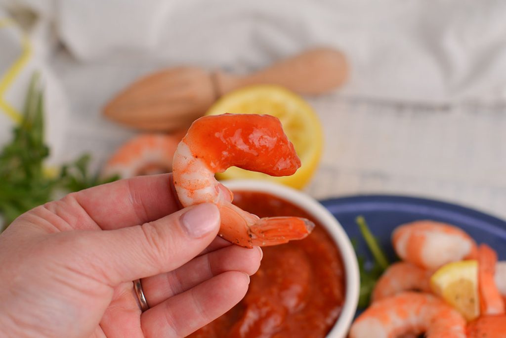 hand holding shrimp dipped in cocktail sauce