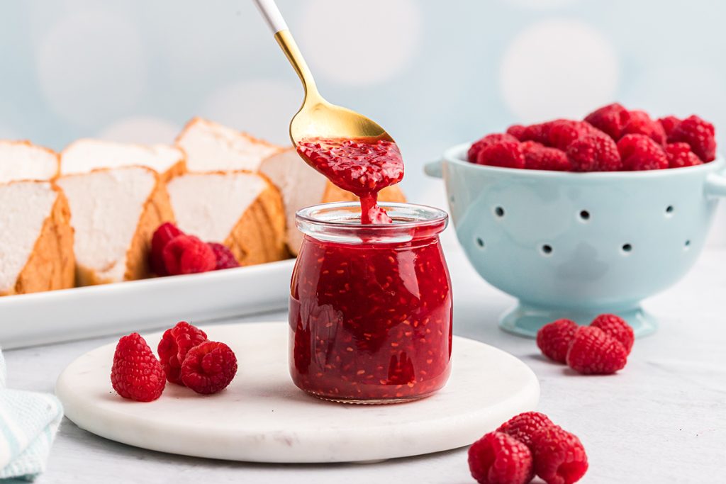 spoon dipping into jar of raspberry sauce
