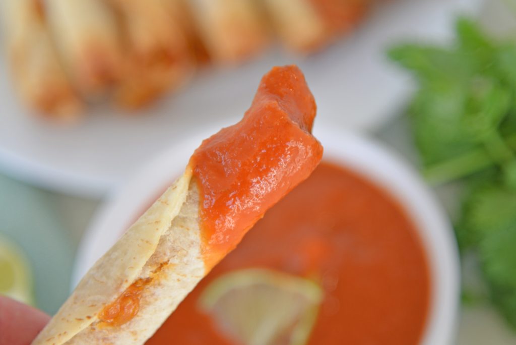 close up of taquito dipped in ranchero sauce