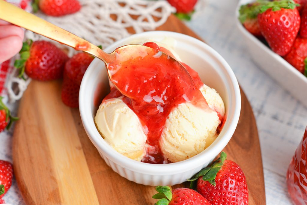 spooning strawberry topping over ice cream
