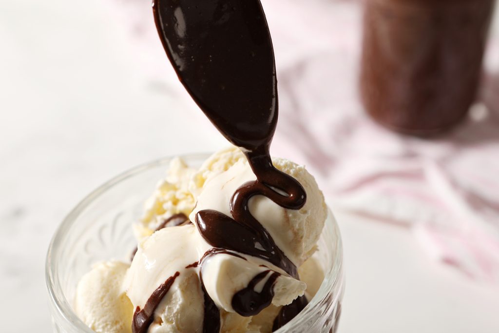 spoon pouring hot fudge over ice cream