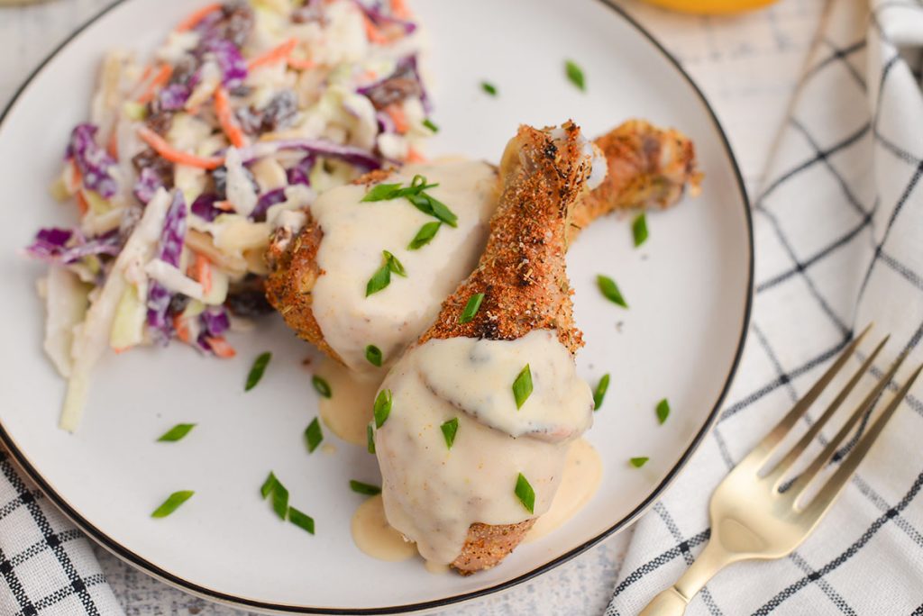 close up of chicken drumsticks on a plate with alabama white sauce and coleslaw