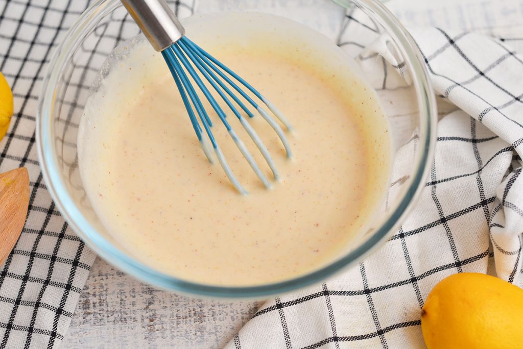 angled shot of alabama white sauce in a bowl with a whisk