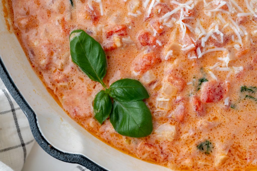 close up of basil leaves in pan of vodka cream sauce