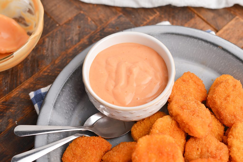 angled shot of bowl of chicken nugget dipping sauce on platter with chicken nuggets