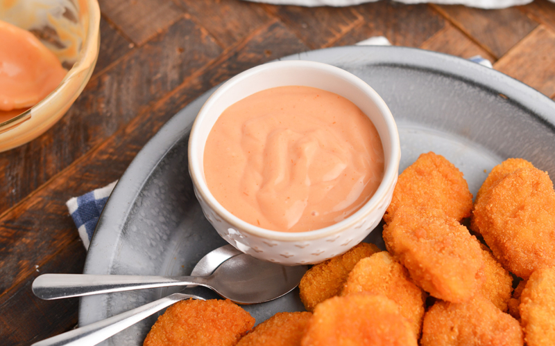 angled shot of bowl of chicken nugget dipping sauce on platter with chicken nuggets