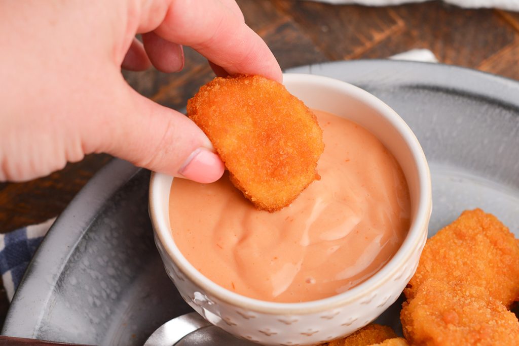 hand dipping chicken nugget into bowl of sauce
