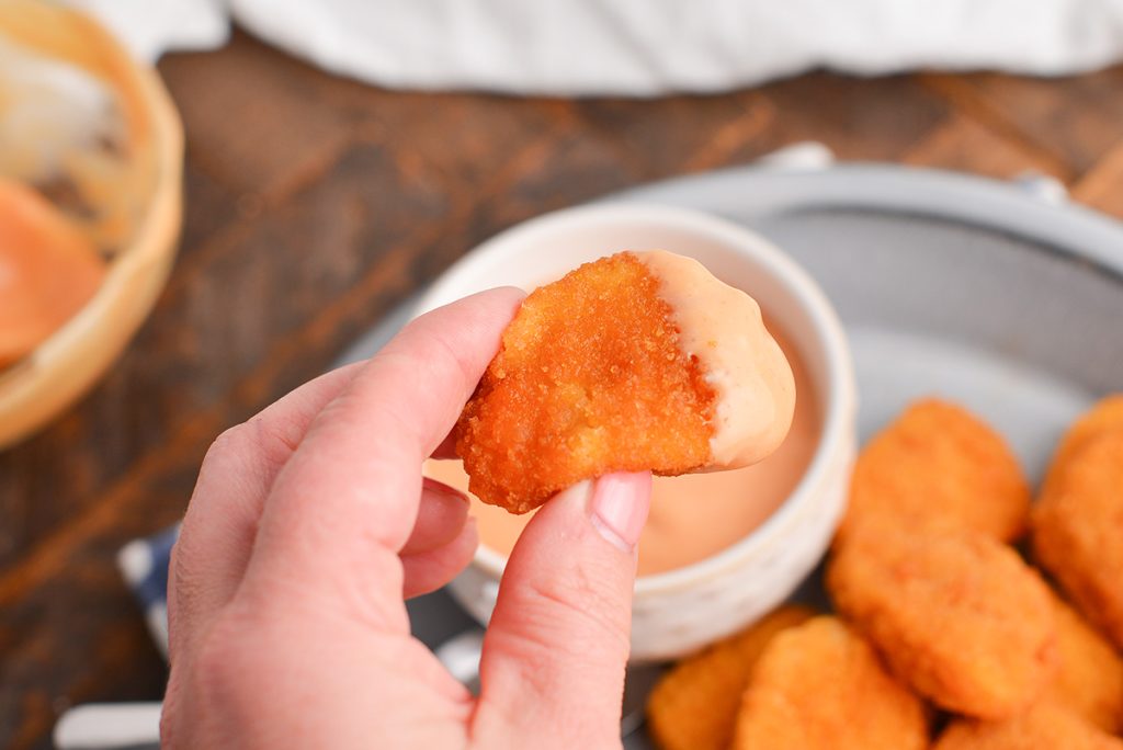 hand holding chicken nugget dipped in sauce