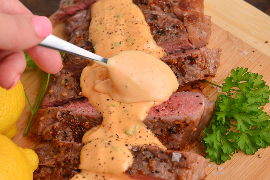 hand spooning french choron sauce onto steak