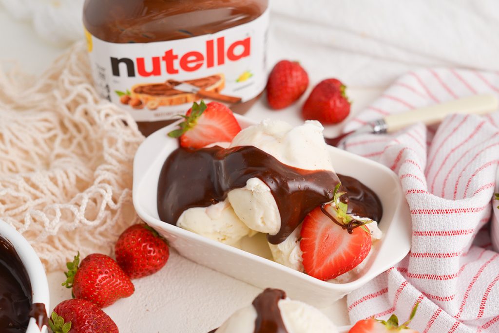 angled shot of nutella sauce on ice cream in a bowl with strawberries