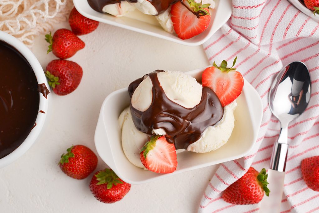 overhead shot of nutella sauce drizzled onto bowl of ice cream with strawberries