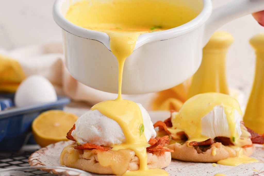 close up shot of hollandaise sauce poured onto eggs benedict