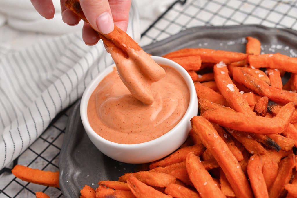 hand dipping sweet potato fried into bowl of sauce