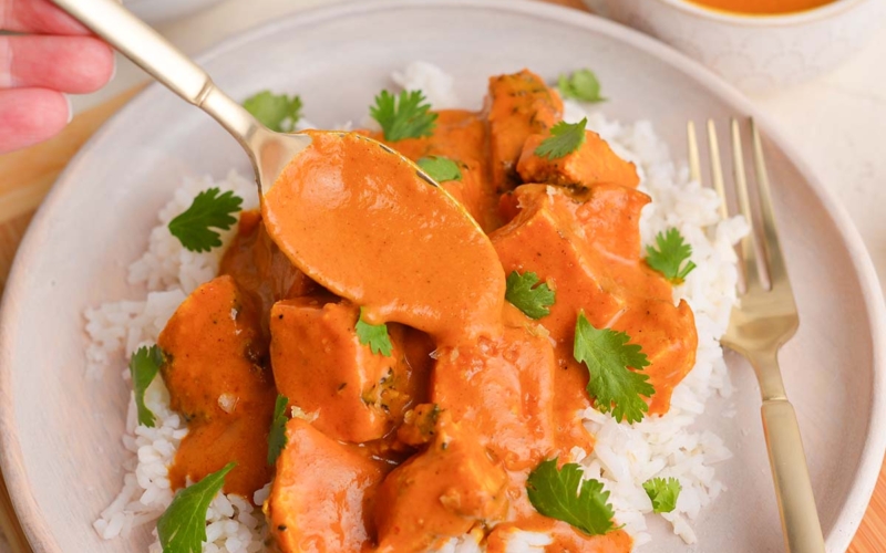 spoon adding curry sauce to chicken