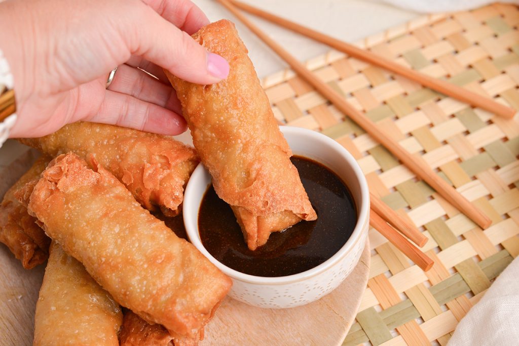 hand dipping egg roll into sauce