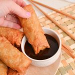hand dipping egg roll into sauce