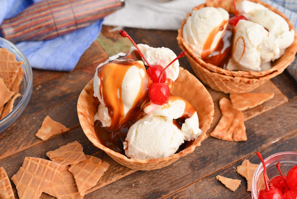 angled shot of ice cream in waffle cone bowl topped with butterscotch sauce