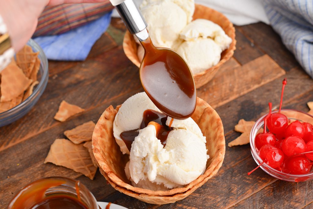 angled shot of spoon drizzling butterscotch sauce on ice cream