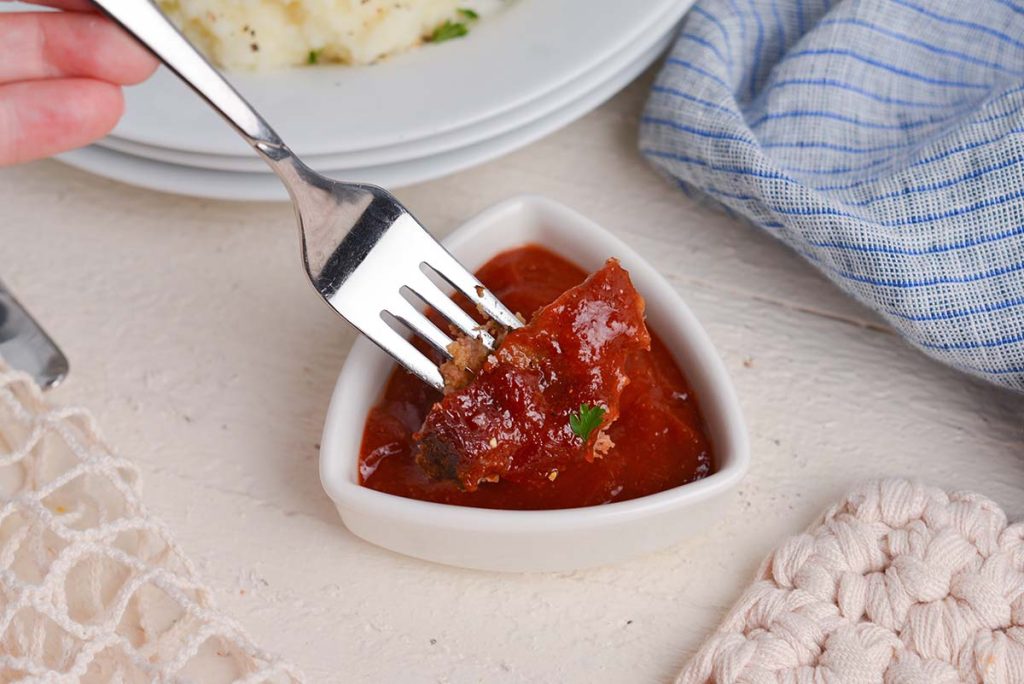 fork dipping bite of meatloaf into meatloaf glaze
