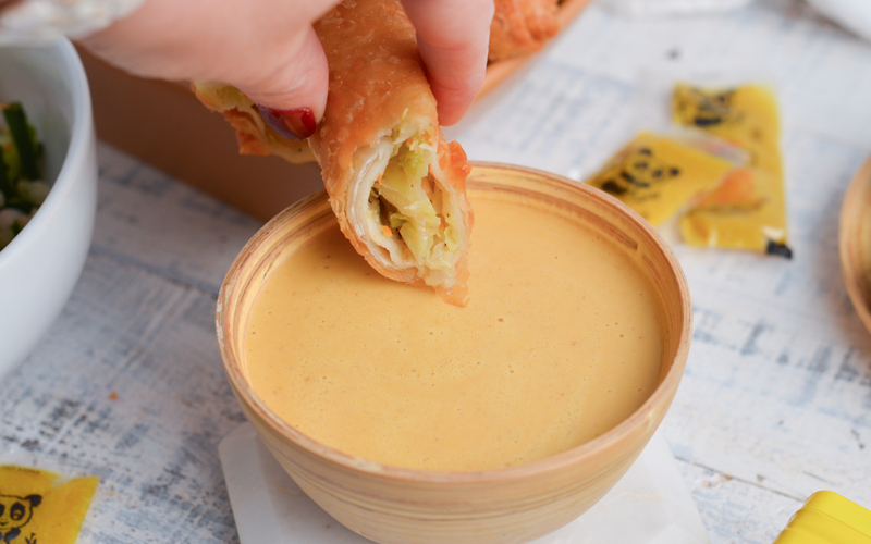 hand dipping egg roll in chinese hot mustard