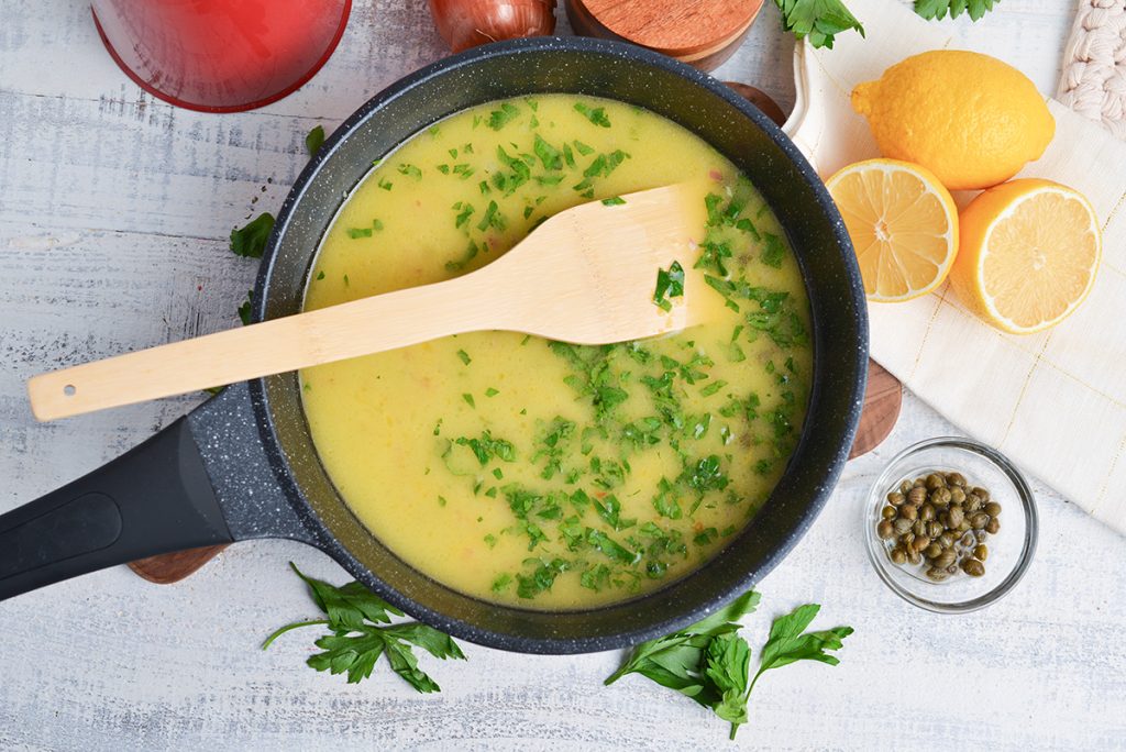 lemon caper sauce in a pan with a wooden spoon