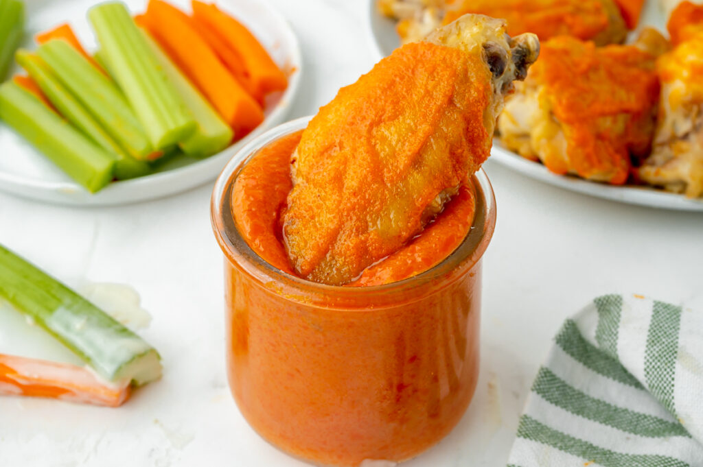 angled shot of chicken wing dipping into homemade buffalo sauce