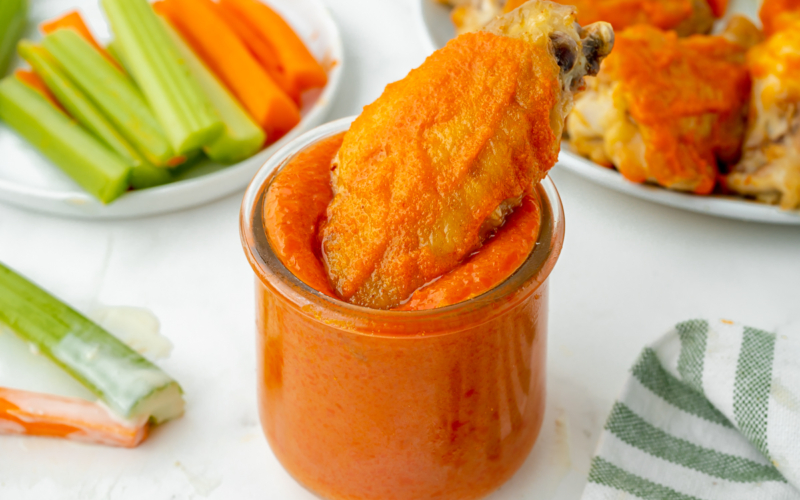 angled shot of chicken wing dipping into homemade buffalo sauce