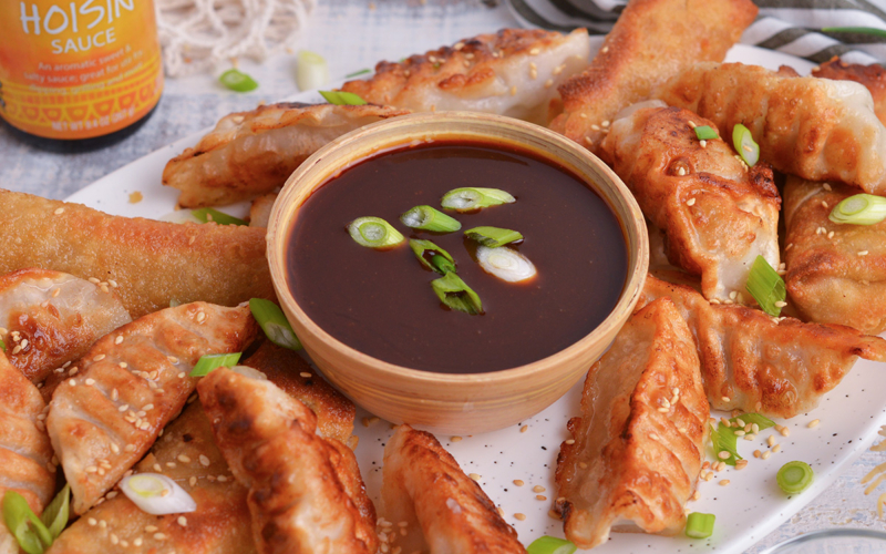 close up angled shot of bowl of homemade hoisin sauce on platter of dumplings