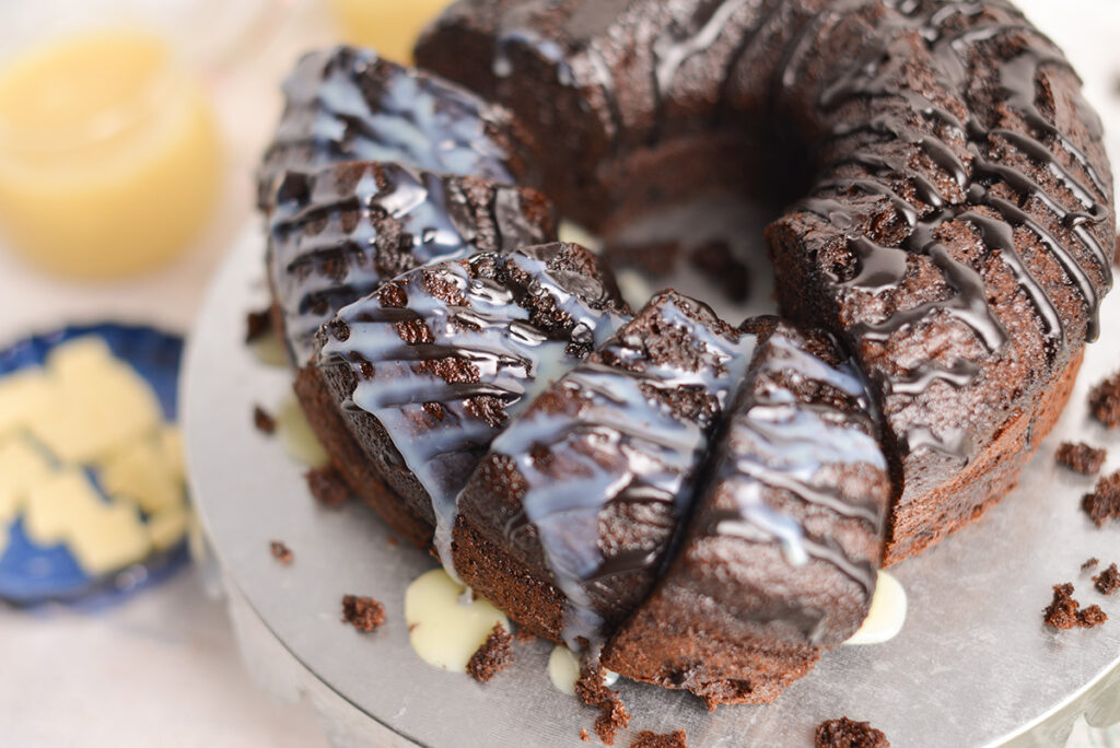 angled shot of chocolate bundt cake topped with white chocolate sauce