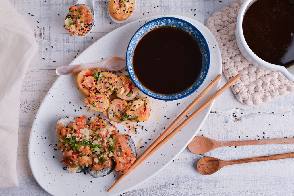 overhead shot of bowl of eel sauce on platter of sushi