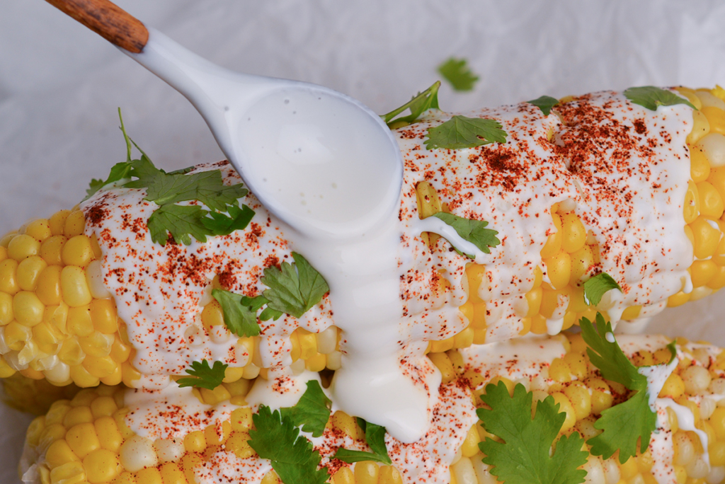 straight on shot of spoon adding mexican crema recipe to corn