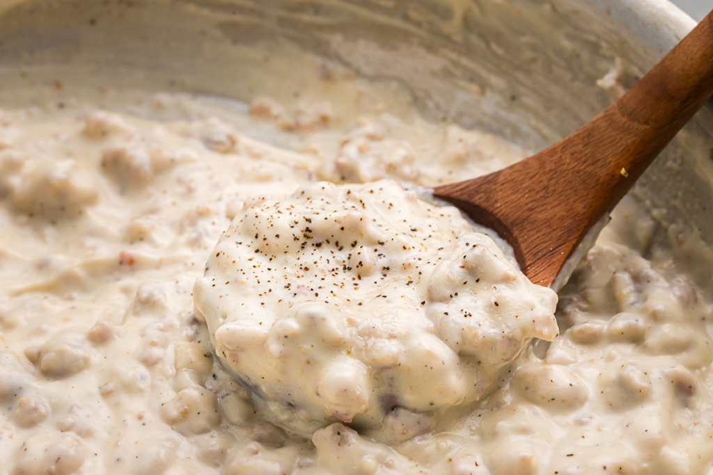 close up angled shot of wooden spoon in pan of country gravy