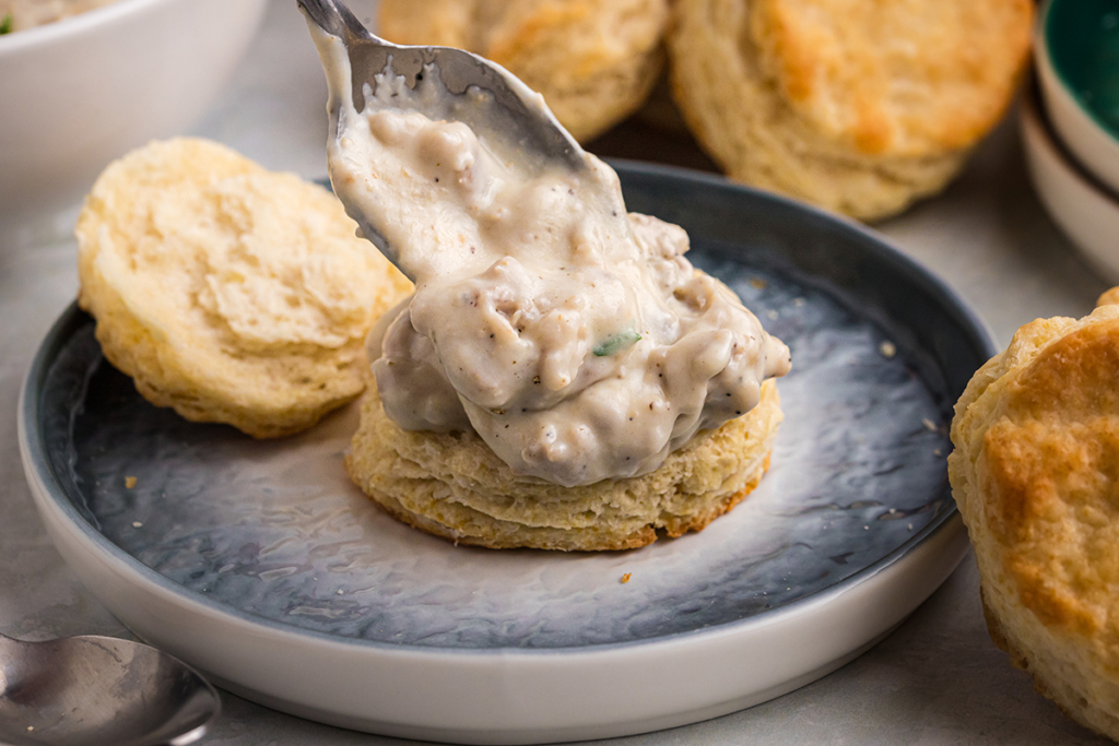 spoon adding country gravy to biscuit