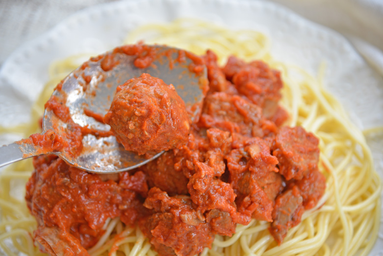 spooning sunday gravy and meatballs over pasta