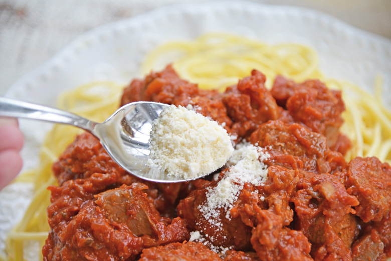 spooning cheese over sunday sauce on pasta