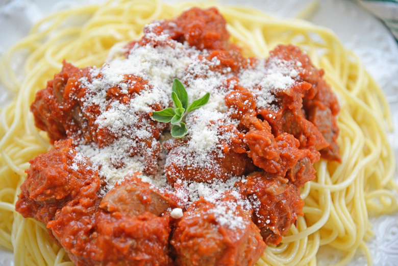 close up angled shot of sunday gravy and meatballs over pasta