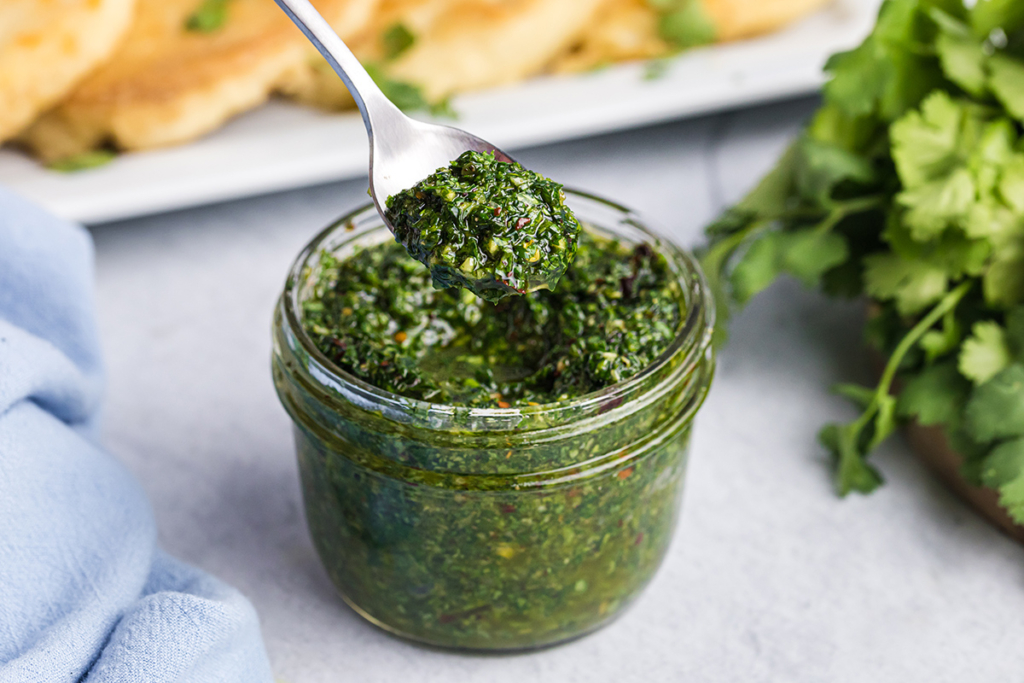 angled shot of spoon in jar of chimichurri sauce