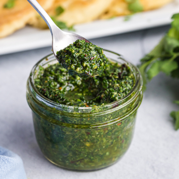 angled shot of spoon in jar of chimichurri sauce