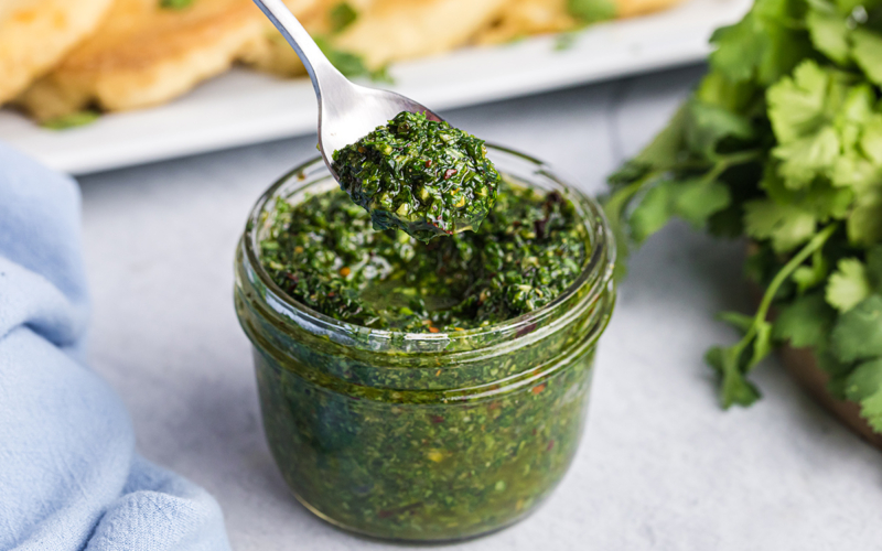 angled shot of spoon in jar of chimichurri sauce