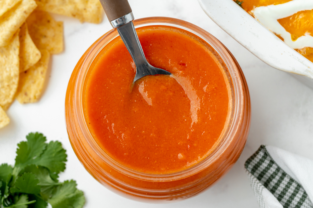 overhead shot of spoon in jar of red enchilada sauce