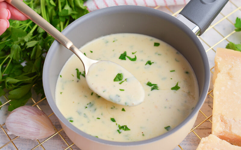 angled shot of spoon in pan of parmesan cheese sauce