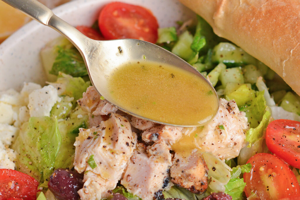 close up shot of spoon adding greek vinaigrette salad dressing to salad