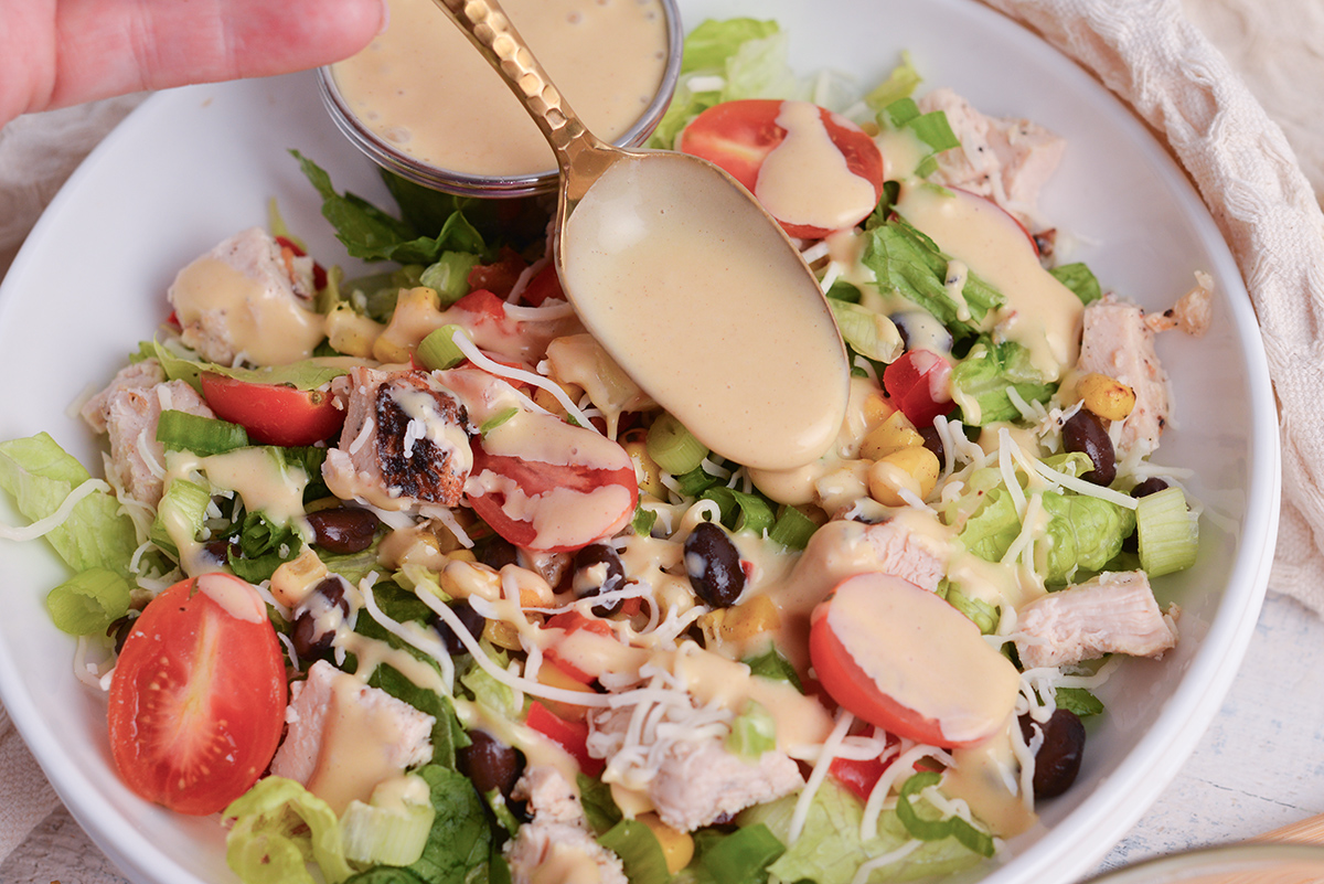 spoon drizzling dressing over salad