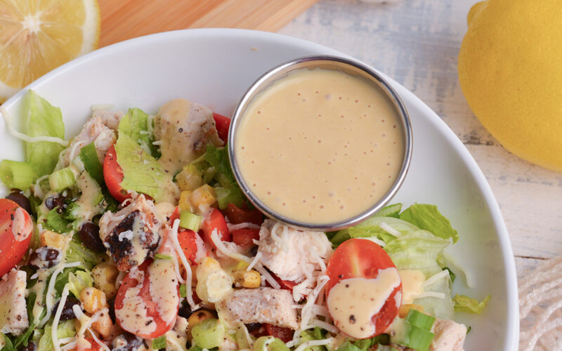 angled shot of ramekin on dressing in bowl of salad