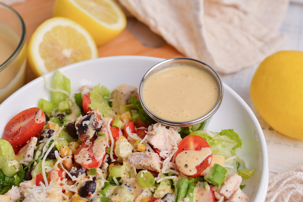 ramekin of honey mustard dressing in bowl of salad