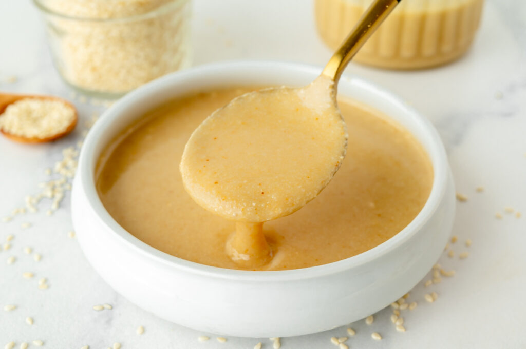 angled shot of spoon dipping into bowl of tahini sauce