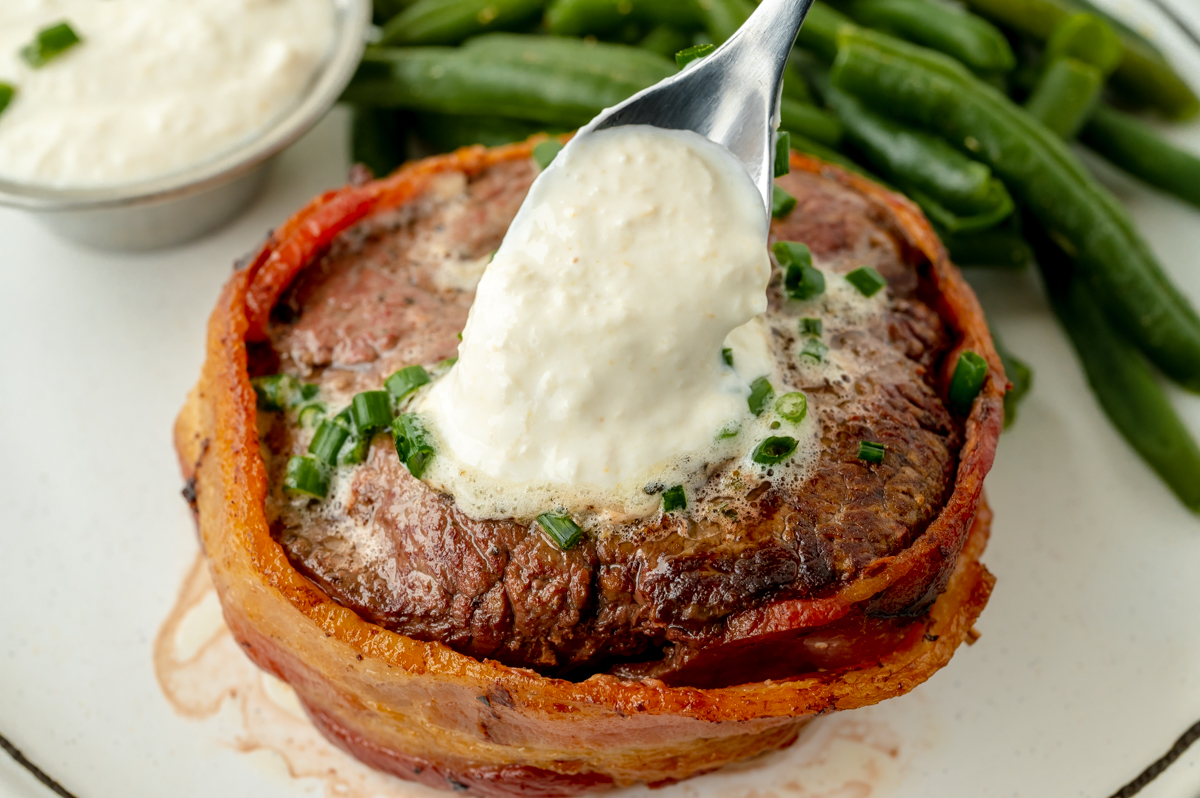 spoon adding creamy horseradish sauce to steak