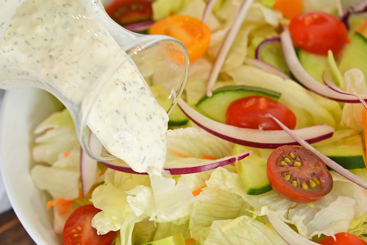 close up of ranch dressing pouring onto salad