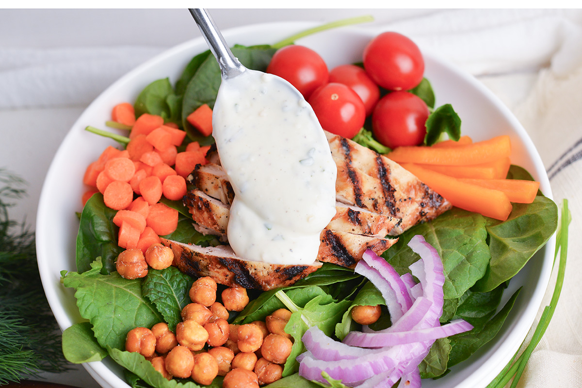 spoon adding dressing to grilled chicken salad